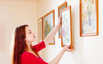 woman in red hanging the art pictures on wall at home