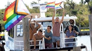 The cast of Fire Island waves rainbow flags from a boat