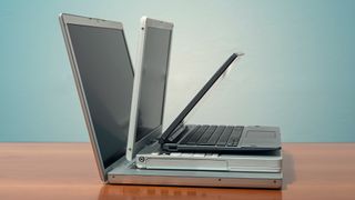 Three pre-used laptops sitting on top of another on a desk.