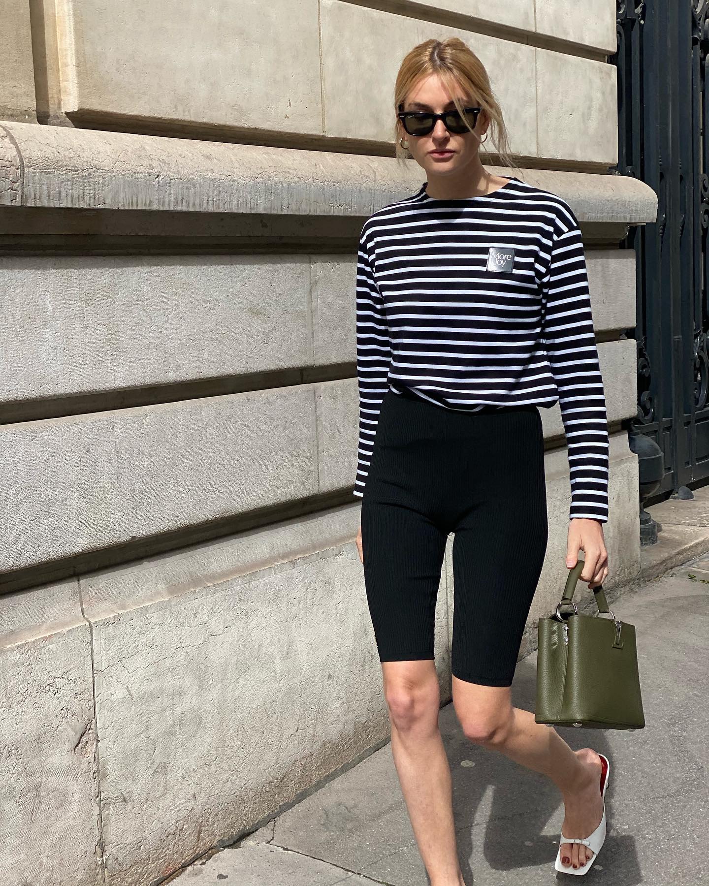 influencer Camille Charrière walks on the sidewalks of Paris wearing a striped long-sleeve tee, black capri pants, green Louis Vuitton bag, and white square-toe mule heels