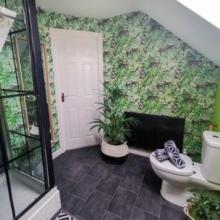Bathroom with grey tiles, plant patterned wall paper, shower, toilet and pot plants