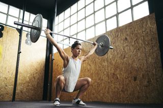 Can I workout after my COVID vaccine? Young brunette woman doing overhead squat exercise at gym