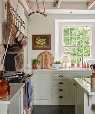 modern farmhouse kitchen with pale green units, a cream range in an old stone fireplace and Georgian sash windows