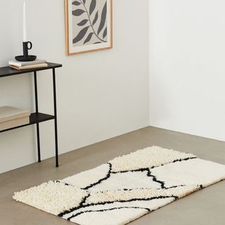 A cream rug sits on a concrete floor, with black cracks serving as its pattern