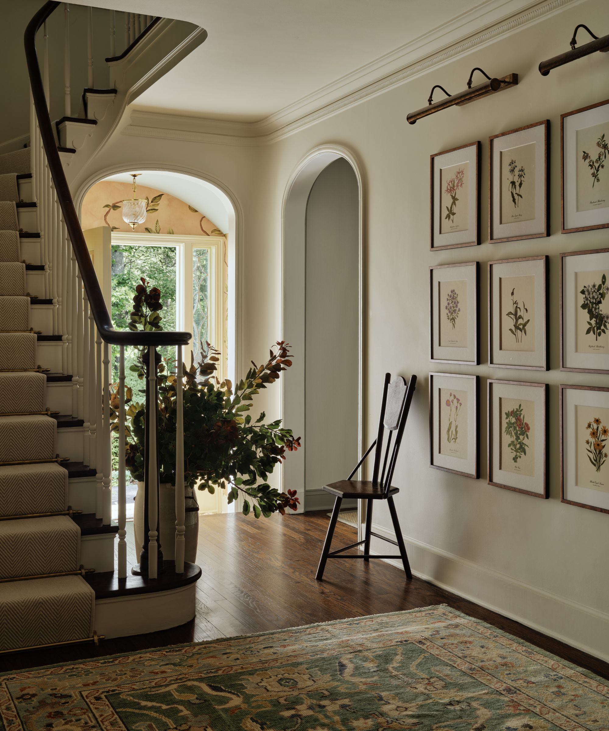 a warm neutral entryway with sweeping staircase, vintage green patterned rug with floral wall art gallery wall
