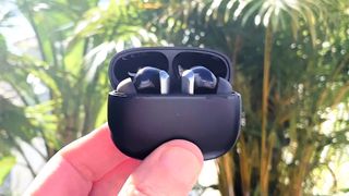 EarFun Air 2 in charging case held between fingers in an outdoor setting with plants in the background