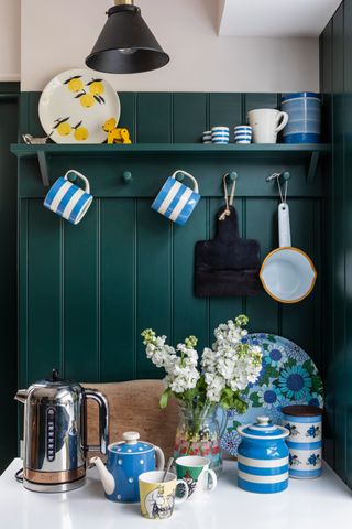 kitchen with green panelled wall and shelf displaying blue and white ceramicware