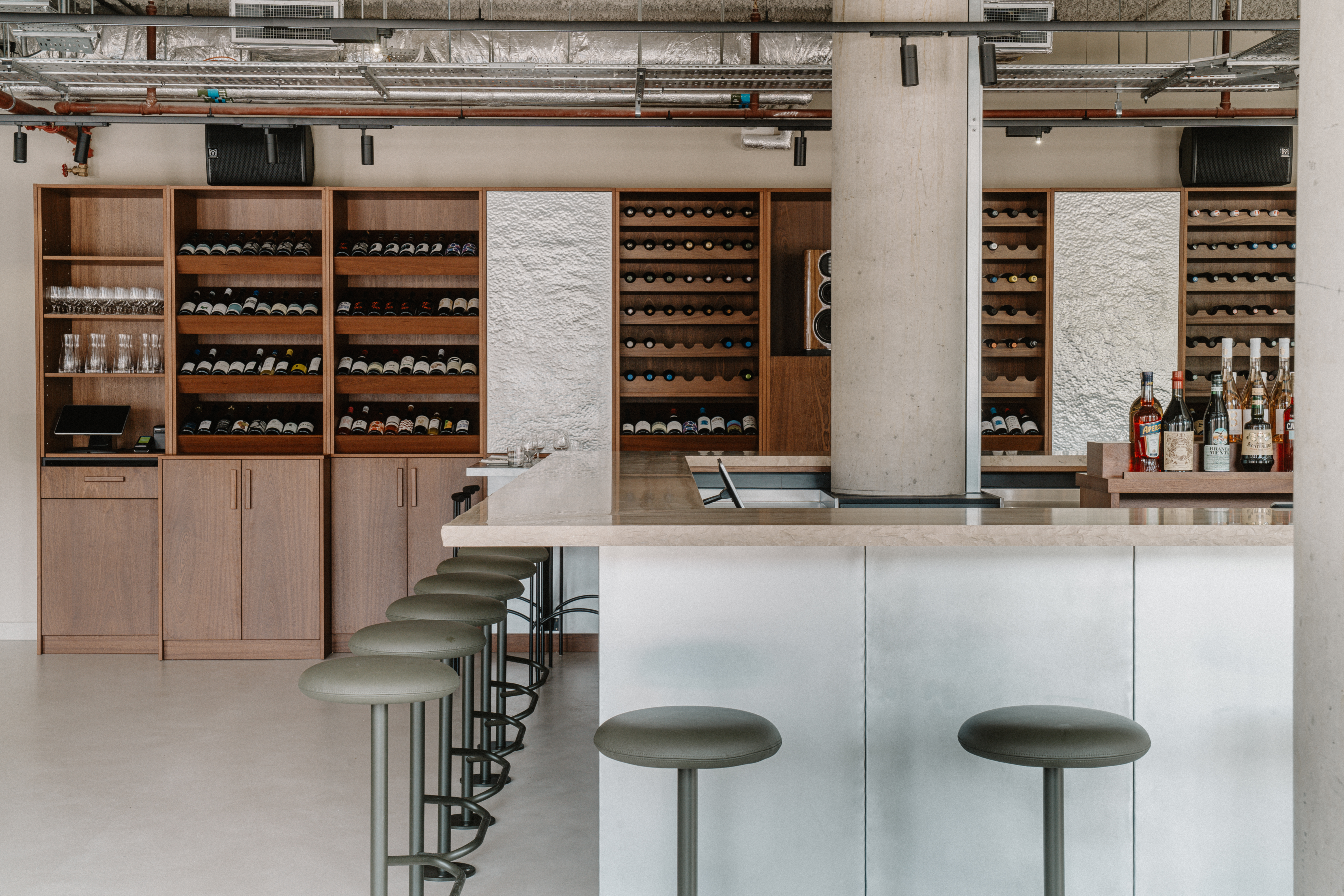 A sun-lit restaurant features brutalist interiors paired with a minimalist, black wrought iron-furnished canal-view terrace.