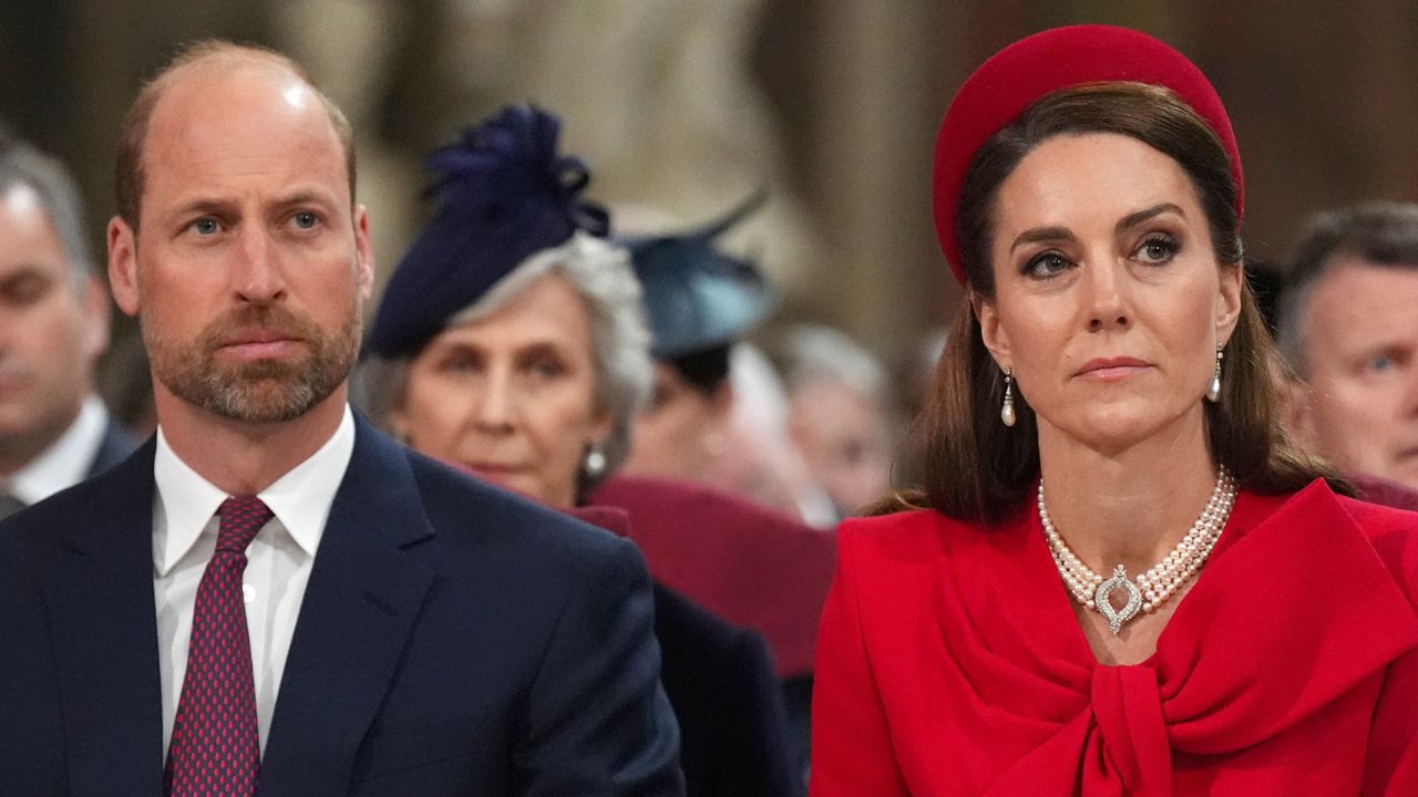 Prince William wearing a suit and a red tie sitting next to Kate Middleton wearing a red coat and hat at Commonwealth Day 2025