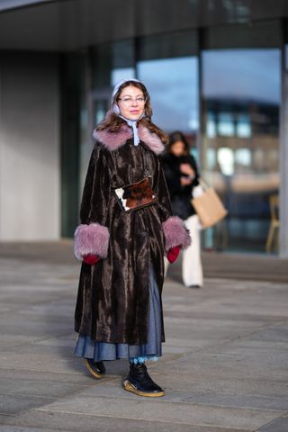 woman wearing a faux fur coat, skirt, head scarf, and sneakers