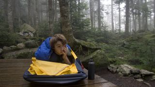 A teenage boy wakes up in a bivvy bag on a wilderness campsite