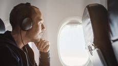 Man on plane listening to travel headphones while looking out of window