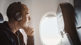 Man on plane listening to travel headphones while looking out of window