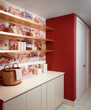 a stylish bold laundry room with colorful wallpaper and floating shelves, and a red wall next to cabinets