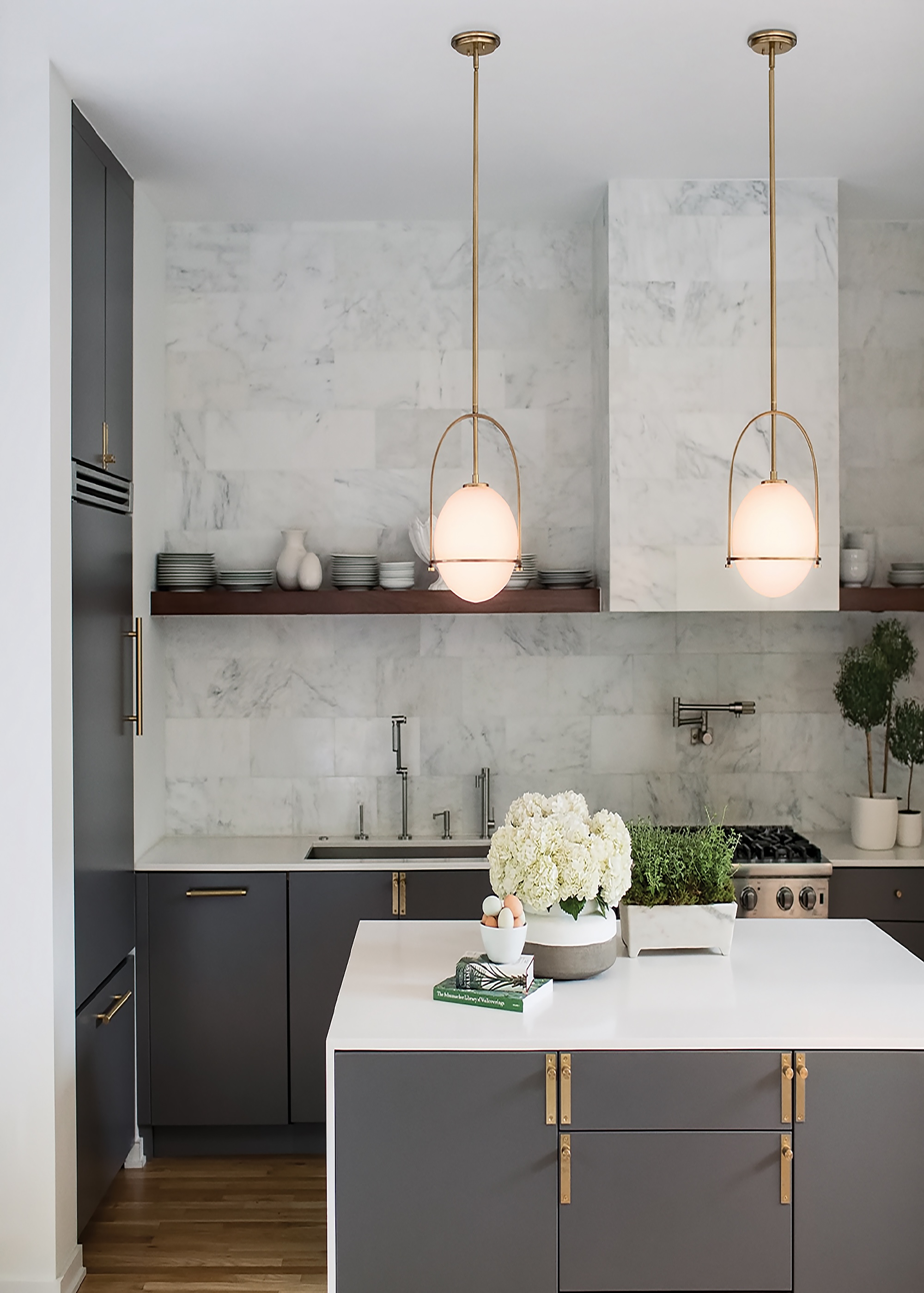 A small grey and white kitchen island in the middle of a small kitchen. Above the island, two pendant lights hang.