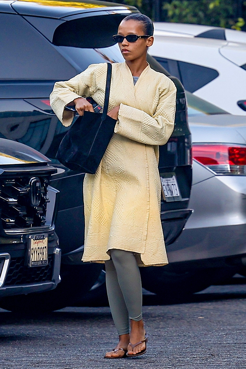 Taylor Russell wearing a butter yellow wrap coat with gray leggings and jelly flip-flops.