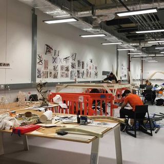 Architecture and engineering students working. We see wooden structures being built, with a lot of sketches on the walls and tables.