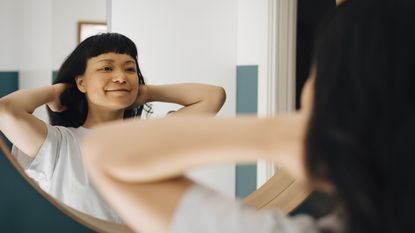 A young woman looks in a mirror and smiles.