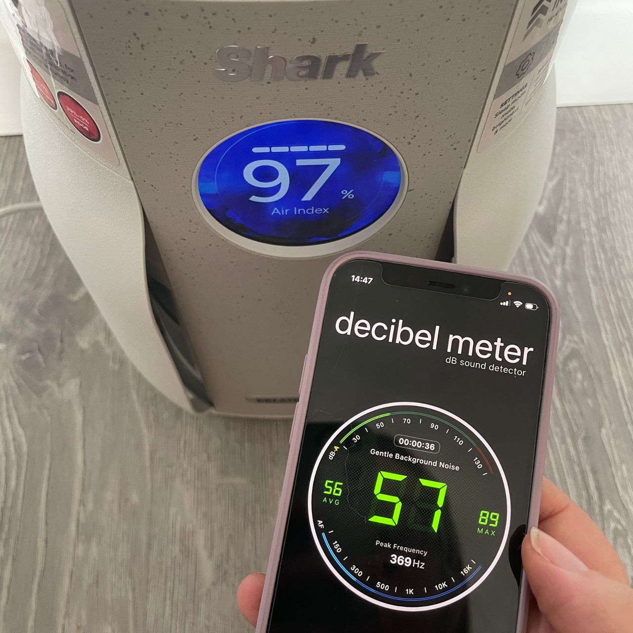 Decibel meter next to a shark air purifier, showing a reading of 57 decibels