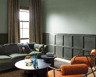 living room with light green upper walls, dark green lower walls and green sofa with orange armchairs