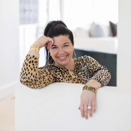 Image of a woman in a leopard print, long sleeve shirt lounging on a white sofa.