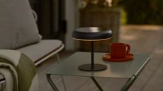 Image of a black outdoor, solar-power table lamp on a green metal table with a red coffee mug next to it.