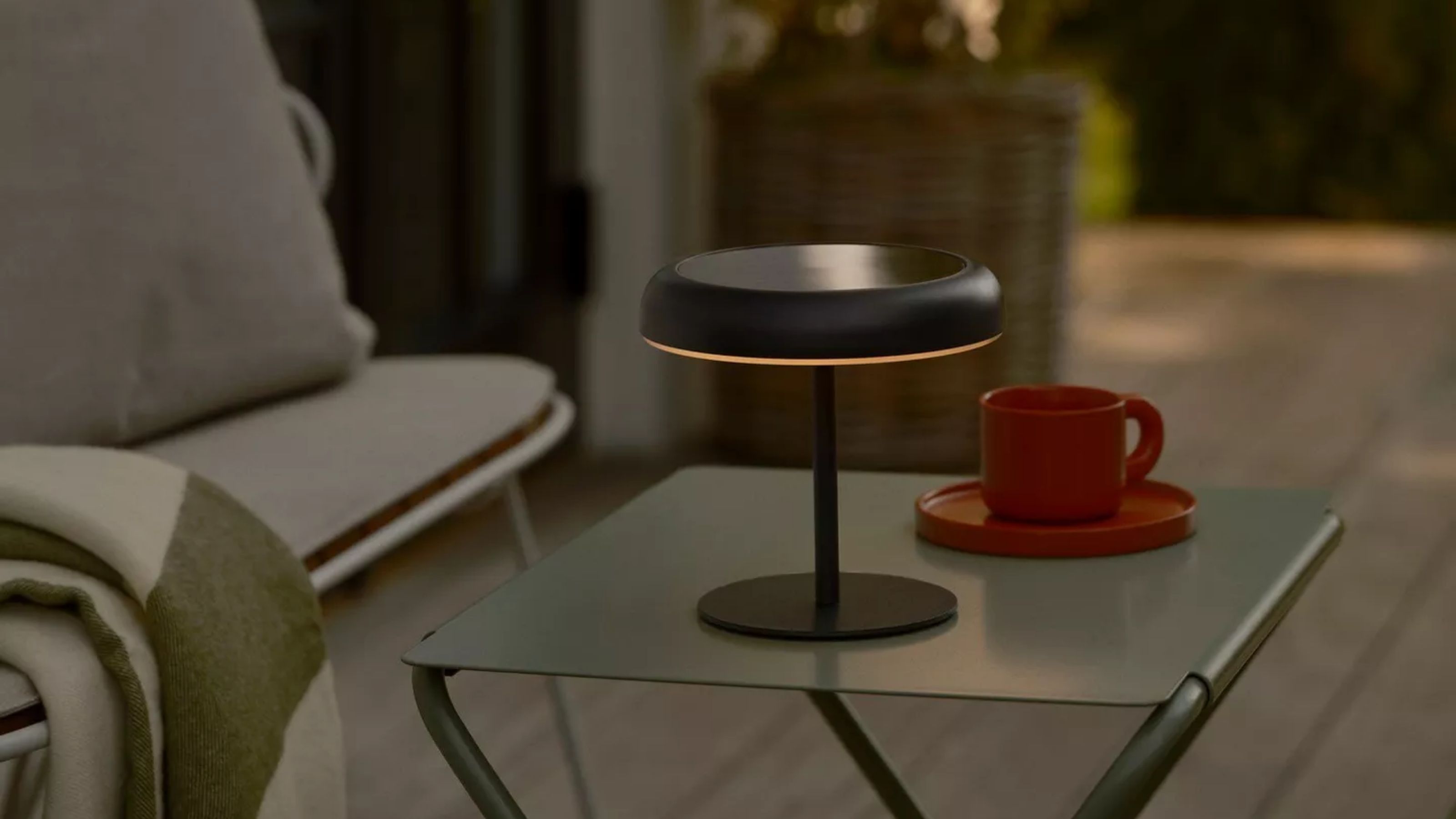 Image of a black outdoor, solar-power table lamp on a green metal table with a red coffee mug next to it.