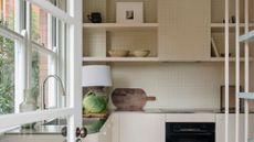 A small kitchen with a tiled backsplash, a head of lettuce on a chopping board and in-built shelving