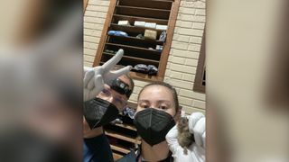 a selfie of two researchers wearing N95 face masks and white gloves, with one holding a bat up to the camera