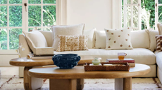 Cream living room with big arched windows, a cream corner sofa with throw pillows and a two wooden coffee tables