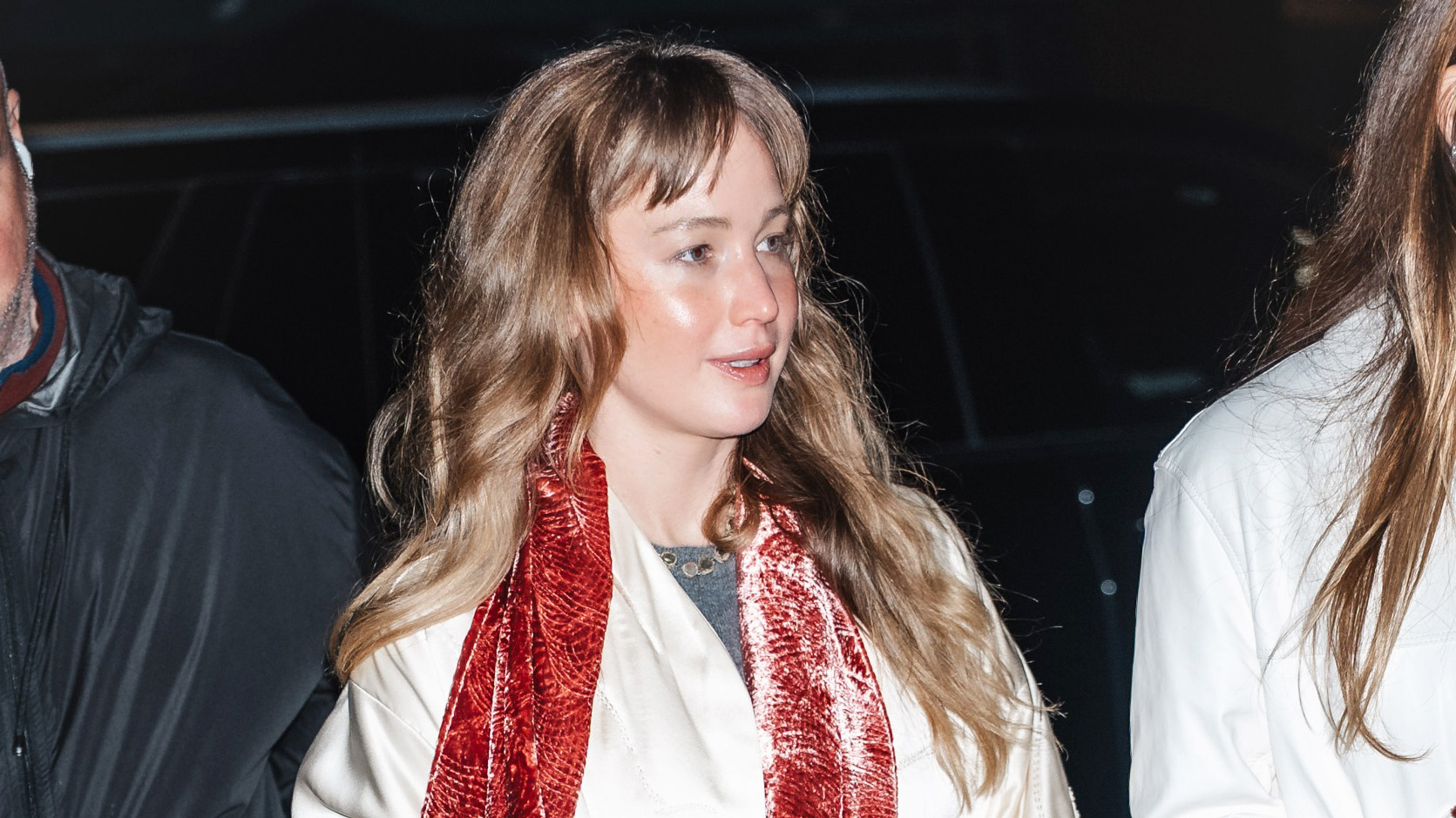Jennifer Lawrence wearing a cream satin coat, jeans, flip-flops, and a pink velvet scarf