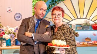 The Great British Bake Off: An Extra Slice hosts Tom Allen and Jo Brand posing with a whisk and a cake