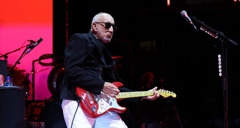 Pete Townshend wears dark shades, a black jacket and white trousers as he plays a red Strat live with the Who in 2025.