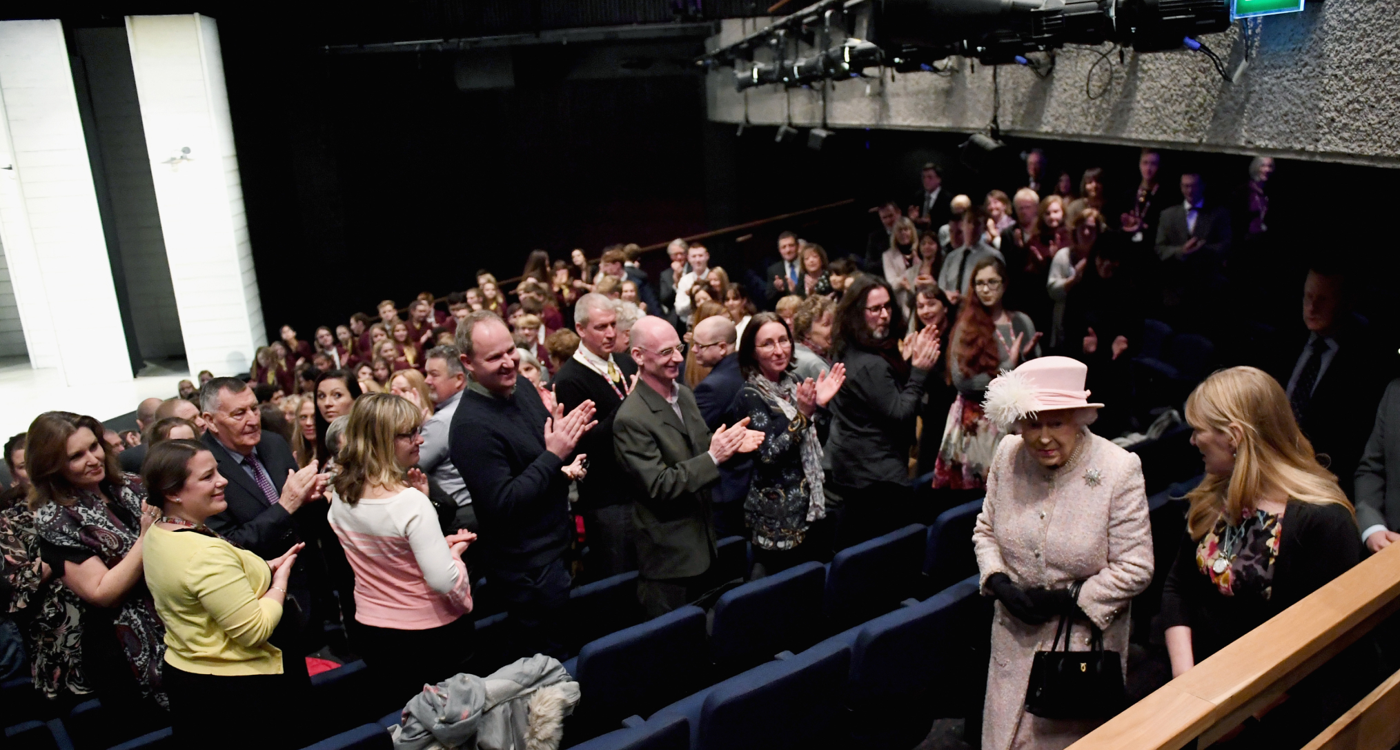 Queen Elizabeth walking into a movie theater and people standing up 