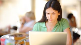 Woman using a laptop in a restaurant terrace with a suspicious look on her face and one eyebrows raised