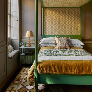 A bedroom with a green four poster bed and mustard bedding and wallpaper