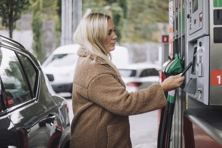 Side view of a woman paying via smart phone while standing at fuel station