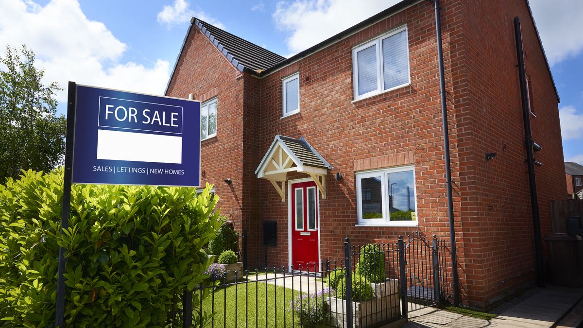 Red brick detached house with double glazing and for sale sign in hedge