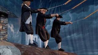 Taylor, Rick, and Drew in revolutionary attire balancing on a log in the middle of a storm while flying a kite. 