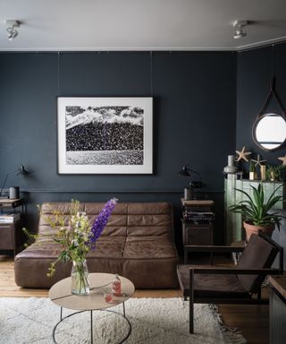 Dark blue painted living room with brown leather sofa and armchair, cream rug over light wood flooring, rounded coffee table, light green tiled fireplace