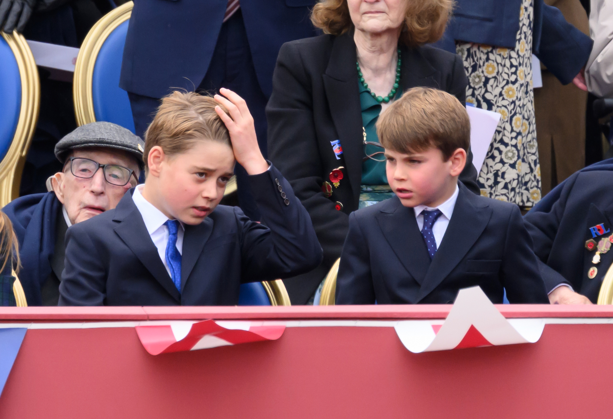 Prince George adjusting his hair at the VE Day parade next to Prince Louis