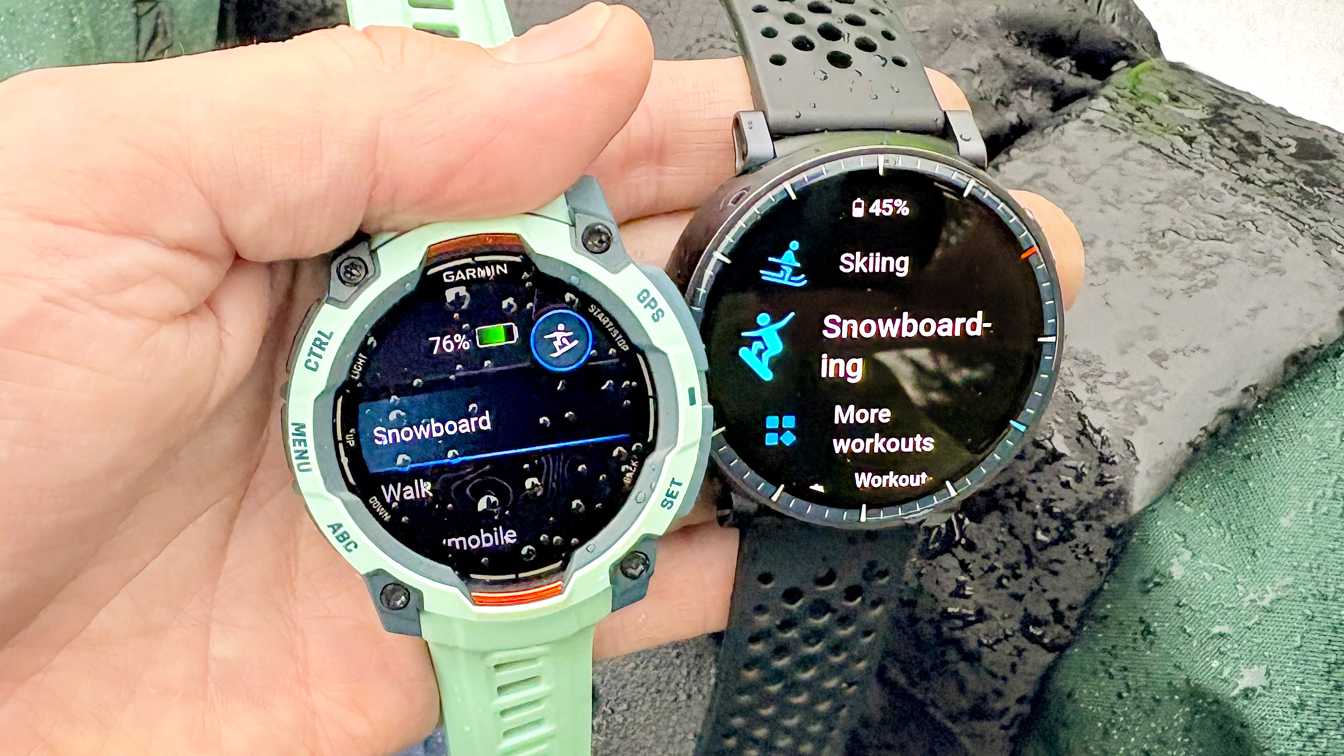 Close-up of the Garmin Instinct 3 and Amazfit Active Max in a user's hand with snow in the background 