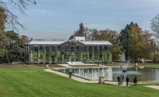 Landscaped lawn and large pond area with fountain sit in front of the contemporary mirrored château