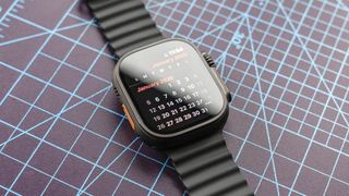 Apple Watch Ultra 2 in Jet Black sitting on a gridded cutting mat showing the 2025 calendar view on the screen