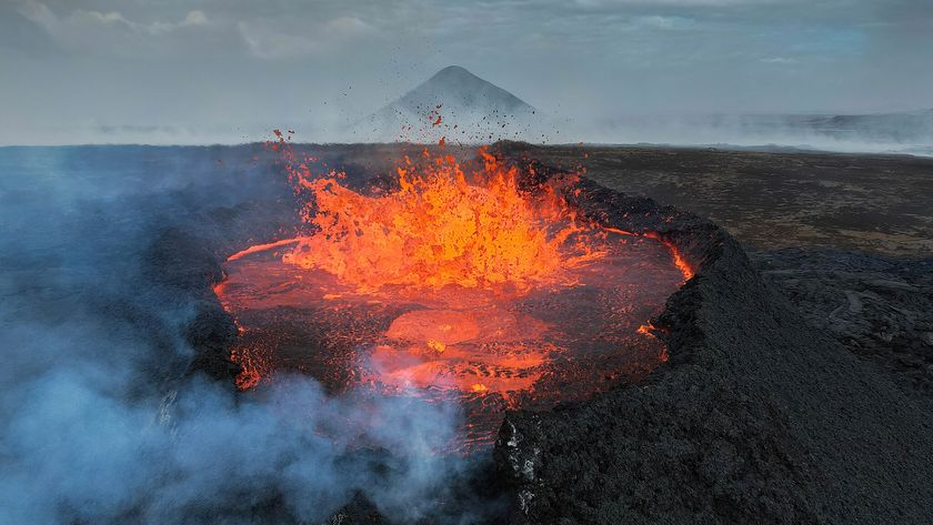 A photograph of a volcanic eruption in Iceland, where a short volcano spews lava into the air with smoke