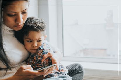 mother looking at phone while hugging child