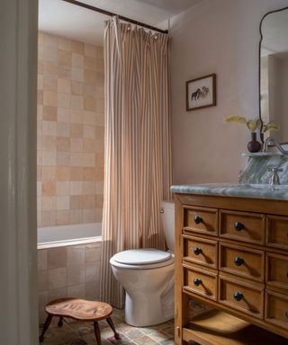 bathroom with neutral walls, earth shower tiles, striped shower curtain and wooden vanity unit