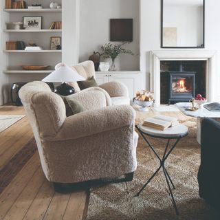 A living room with wooden floorboards and a jute rug with two teddy cream armchairs on top