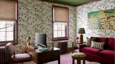 Home office with floral wallpaper, green ceiling, vintage wooden desk, burgundy velvet sofa, and a vibrant pink rug.