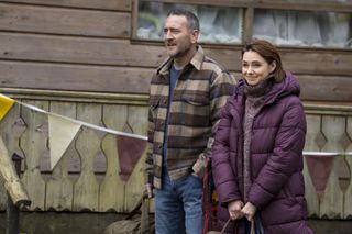 Jimmy (Will Mellor) and Dani (Kara Tointon) stand together outside a log cabin as Jimmy gives instructions to their pupils (who are out of shot). They are both smiling.